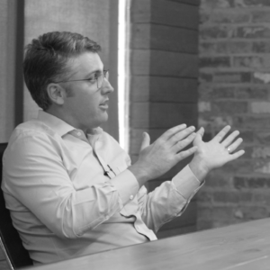 Chris Powers in a white button down using his hands to explain something.