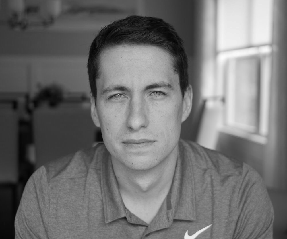 Headshot of Nick Huber, smiling in a collared shirt and tie with an orange microphone to the left of the image