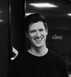 Headshot of Andrew Farah, smiling in a collared shirt and tie with an orange microphone to the left of the image