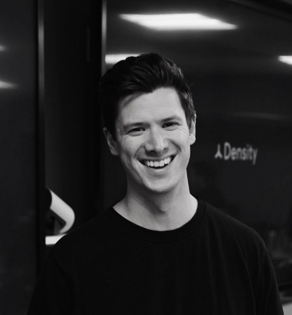 Headshot of Andrew Farah, smiling in a collared shirt and tie with an orange microphone to the left of the image
