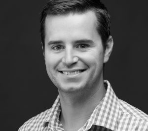 Headshot of Andrew Segal, smiling in a collared shirt and tie with an orange microphone to the left of the image